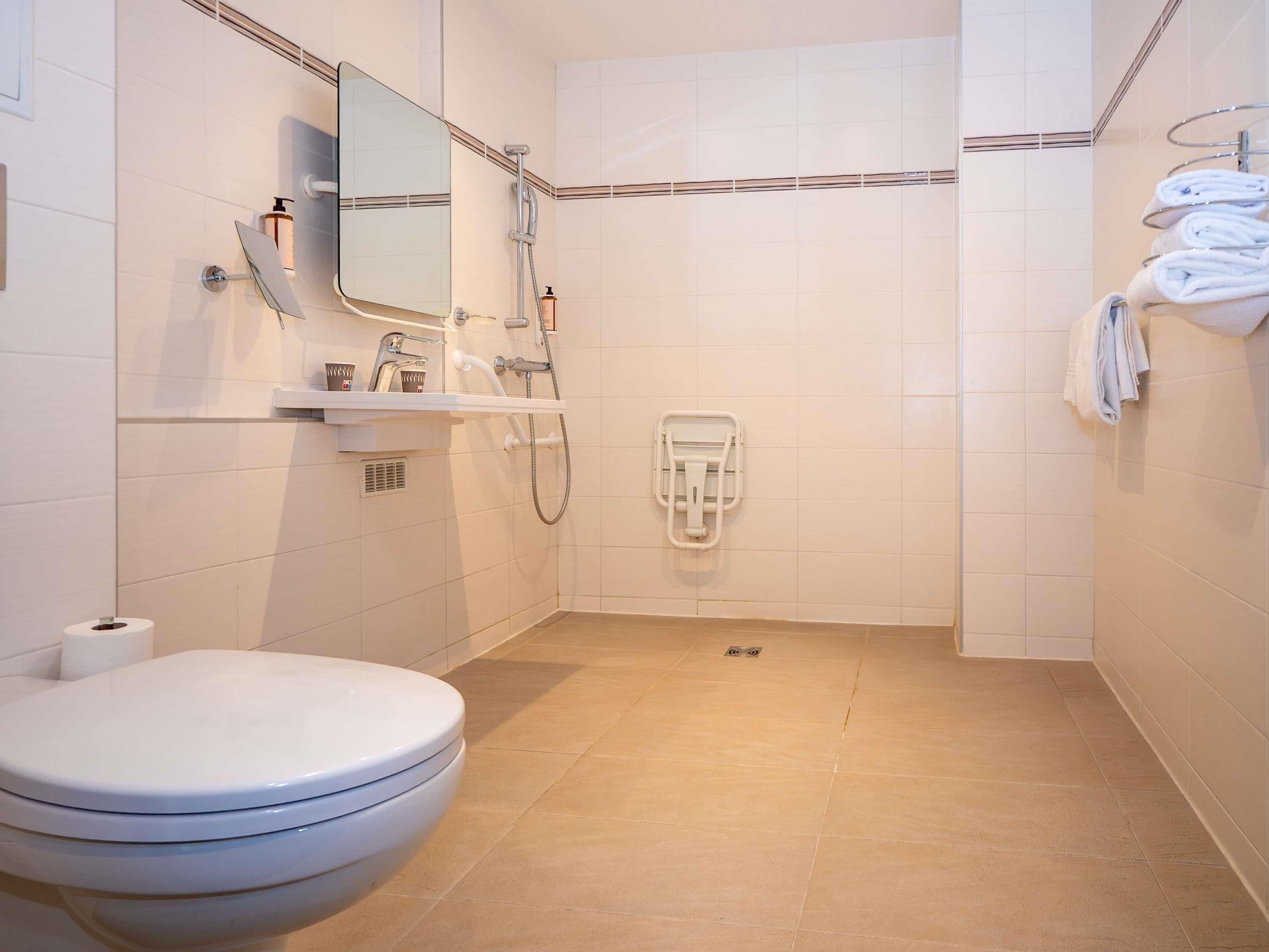 A modern bathroom with a toilet, sink, mirror, shower, and towel rack.