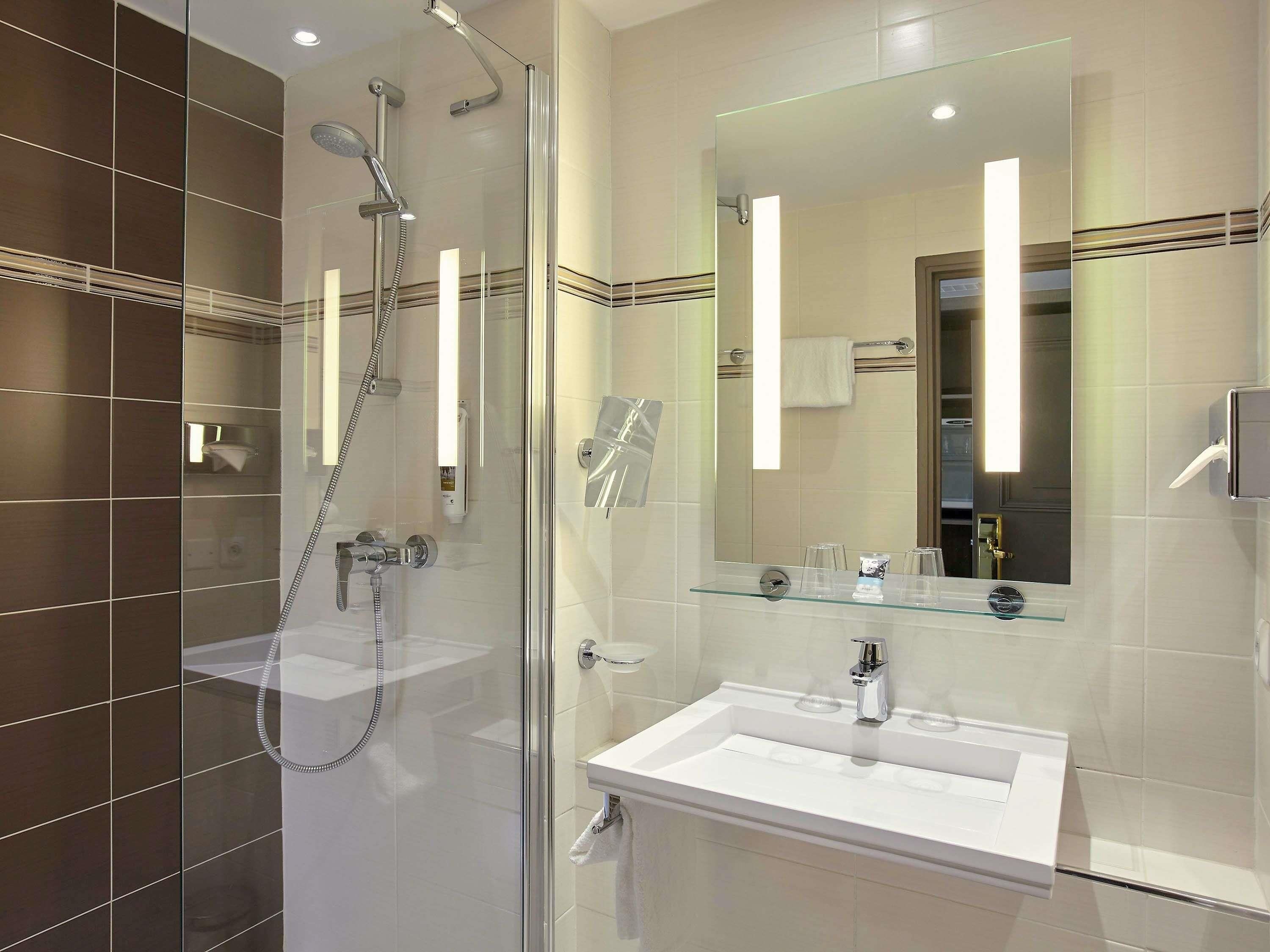 A modern bathroom with a glass-enclosed shower, a white sink, and a large mirror.