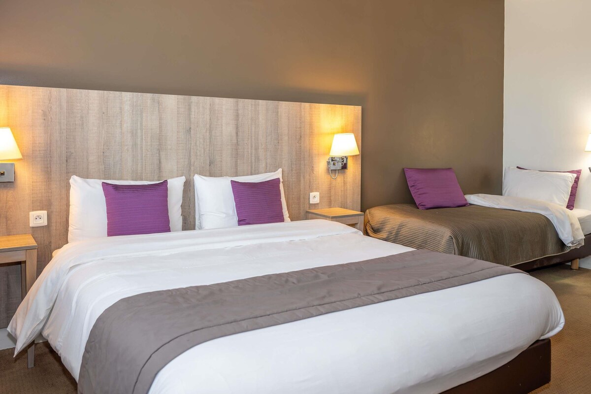 A hotel room with two beds, each with a headboard, bedside lamps, and pillows.