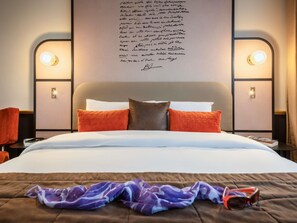 A hotel room with a bed, pillows, a blanket, a pair of sunglasses, and a wall with a light fixture and a handwritten note. - Mercure Versailles Paris Ouest (Le Chesnay-Rocquencourt)