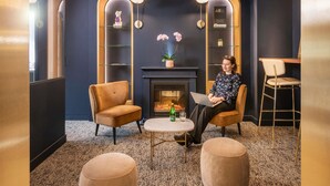 A modern lounge with a fireplace, two armchairs, a round coffee table, and a bookshelf. - Mercure Versailles Paris Ouest (Le Chesnay-Rocquencourt)