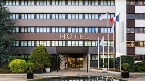 A modern hotel with a prominent entrance, multiple flags, and well-maintained landscaping. - Mercure Versailles Paris Ouest (Le Chesnay-Rocquencourt)