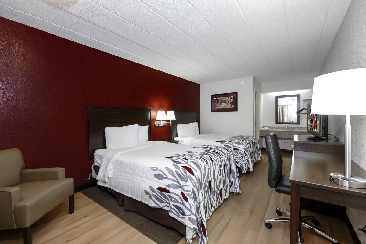 A hotel room with two beds, a desk, a chair, and a TV.
