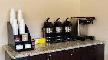 A coffee station with disposable cups, a coffee machine, and a coffee pot.