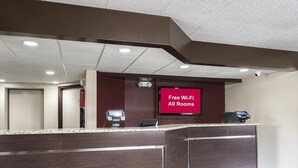 A reception desk with a digital screen displaying 'Free Wi-Fi All Rooms'. - Red Roof Inn Chicago-O'Hare Airport/ Arlington Hts (Arlington Heights)