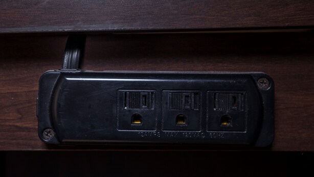 Un enchufe eléctrico negro con tres tomas, situado en un cajón de madera.