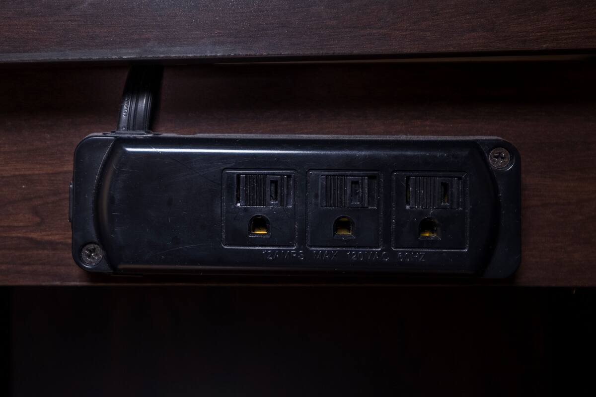 Una presa elèctrica negra amb tres orificis, situada en un calaix de fusta.