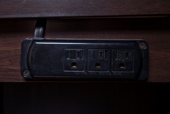 Un enchufe eléctrico negro con tres tomas, situado en un cajón de madera.