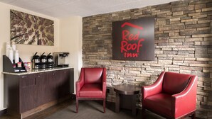 A Red Roof Inn reception area with a stone wall, a coffee station, and two red chairs. - Red Roof Inn Chicago-O'Hare Airport/ Arlington Hts (Arlington Heights)
