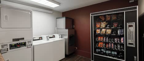A compact kitchen area with a refrigerator, a washing machine, and a vending machine.
