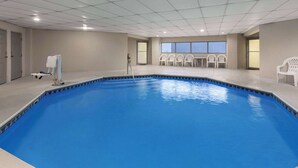 Ein Hallenbad mit blauem Boden, weißen Stühlen und einem Rettungsschwimmerstand.