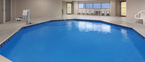 An indoor swimming pool with a blue floor, white chairs, and a lifeguard stand.