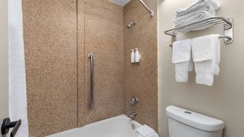 Ein Badezimmer mit Badewanne, Dusche und Toilette. Handtücher und Pflegeprodukte befinden sich an der Wand.