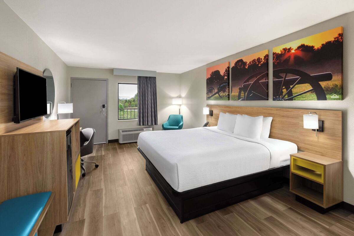 A hotel room with a bed, a desk, a television, and artwork on the wall.