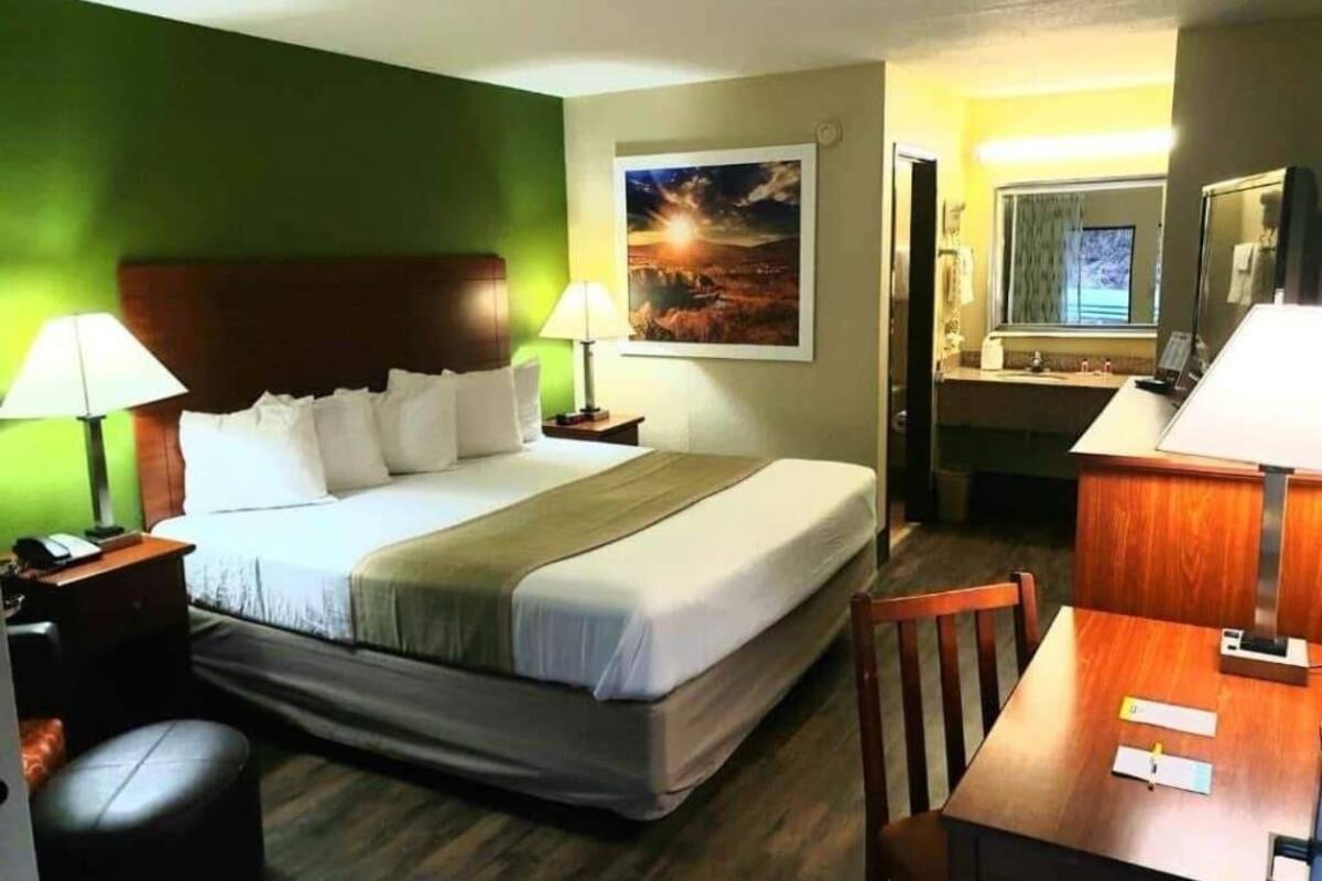 A hotel room with a bed, a desk, a chair, a lamp, a painting, and a window.
