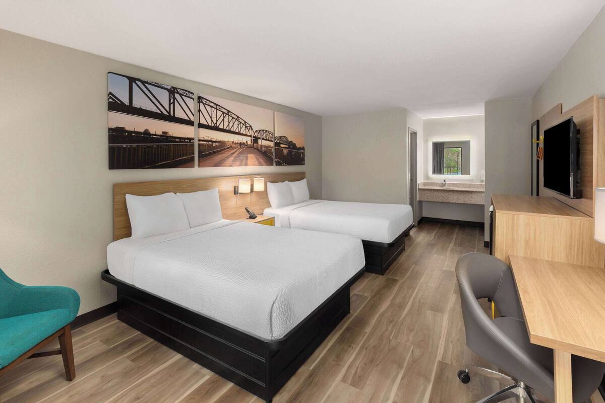 A hotel room with two beds, a desk, a TV, and a large window.