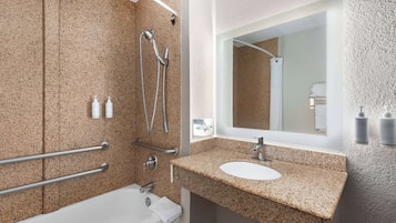 Un bany modern amb un lavabo de superfície de granit, un mirall gran i una zona de dutxa amb barres de sujeció.