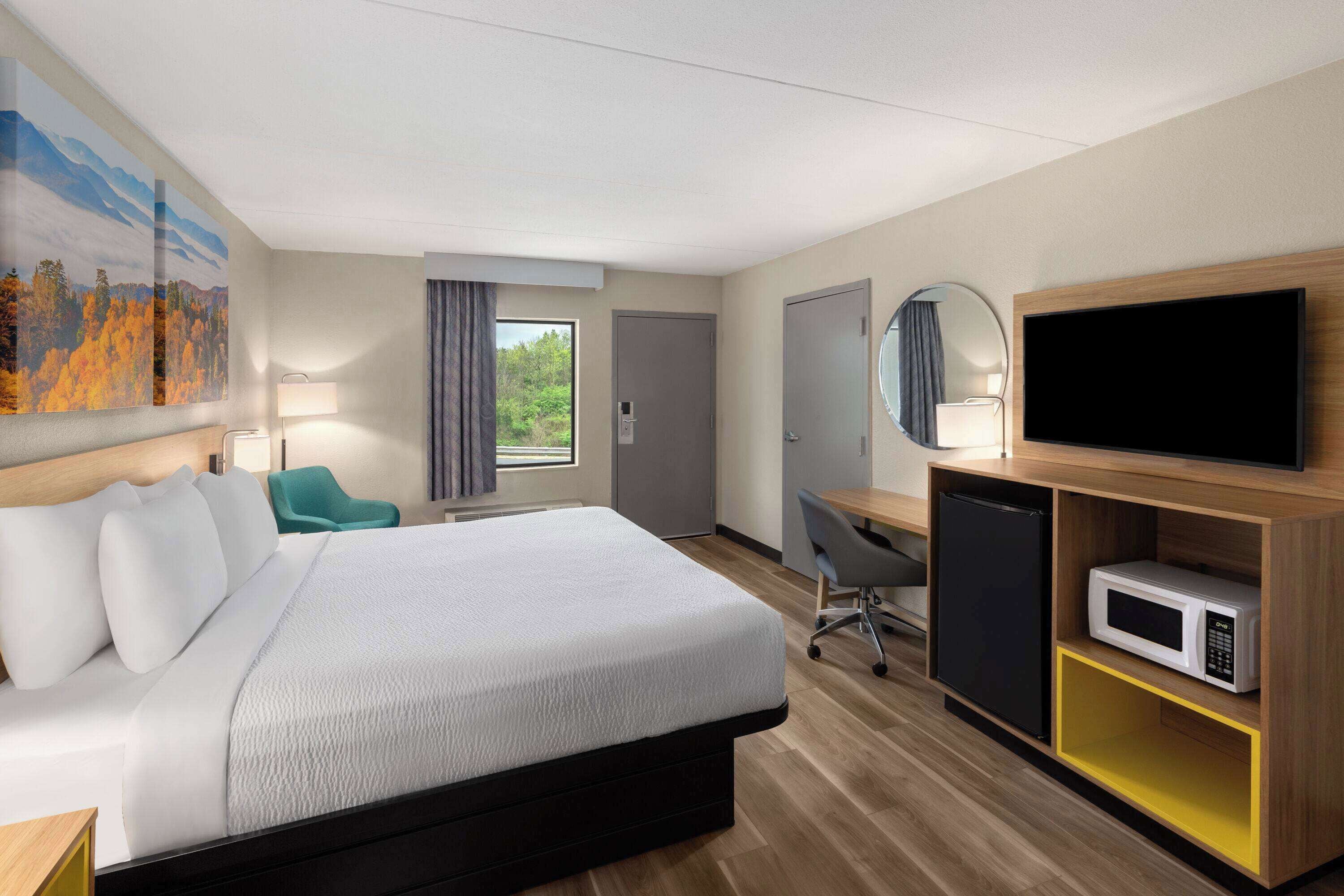 A hotel room with a large bed, a desk with a computer, a TV, a microwave, and a small fridge.