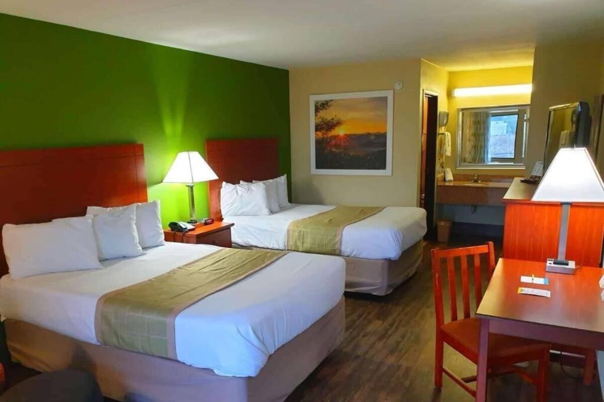 A hotel room with two beds, a desk, a chair, a mirror, and a painting on the wall.