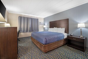 A hotel room with a bed, bedside tables, a desk, and a shower curtain. - Econo Lodge Hicksville - Long Island (Hicksville)