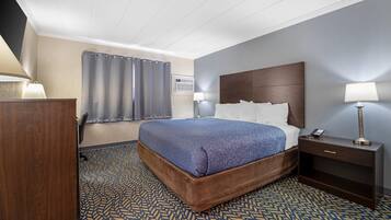 Quarto de hotel com cama, mesas de cabeceira, escrivaninha e tapete estampado.