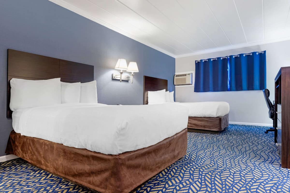 A hotel room with a large bed, a smaller bed, a desk, and a blue patterned carpet.