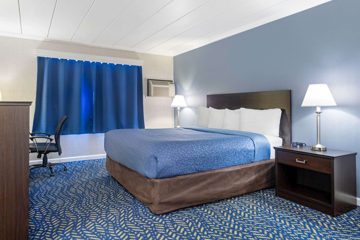 A hotel room with a bed, two bedside lamps, a desk with a lamp, a chair, and a blue curtain.