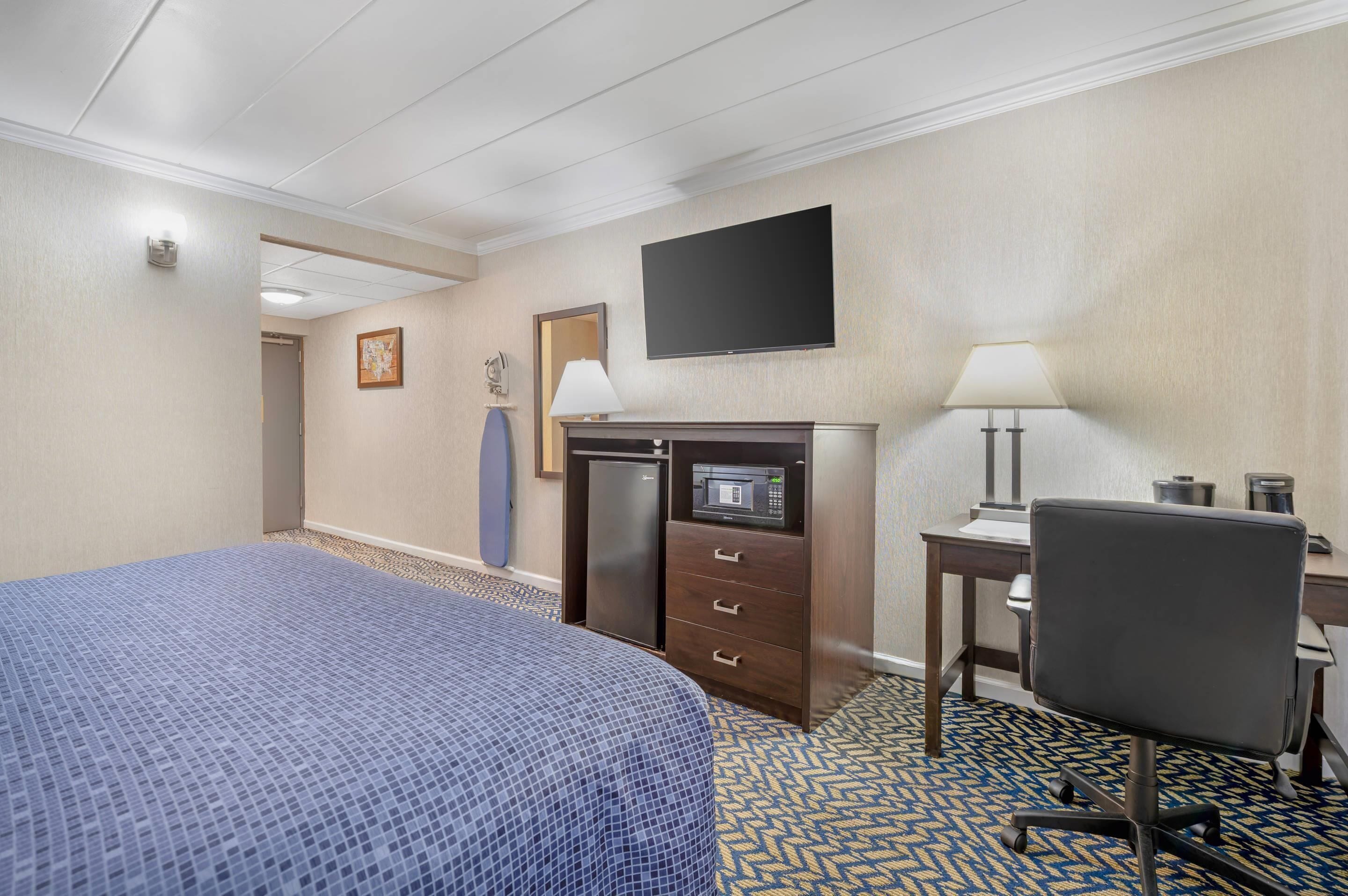 Una habitación de hotel con cama, escritorio, silla, televisión, refrigerador y microondas.