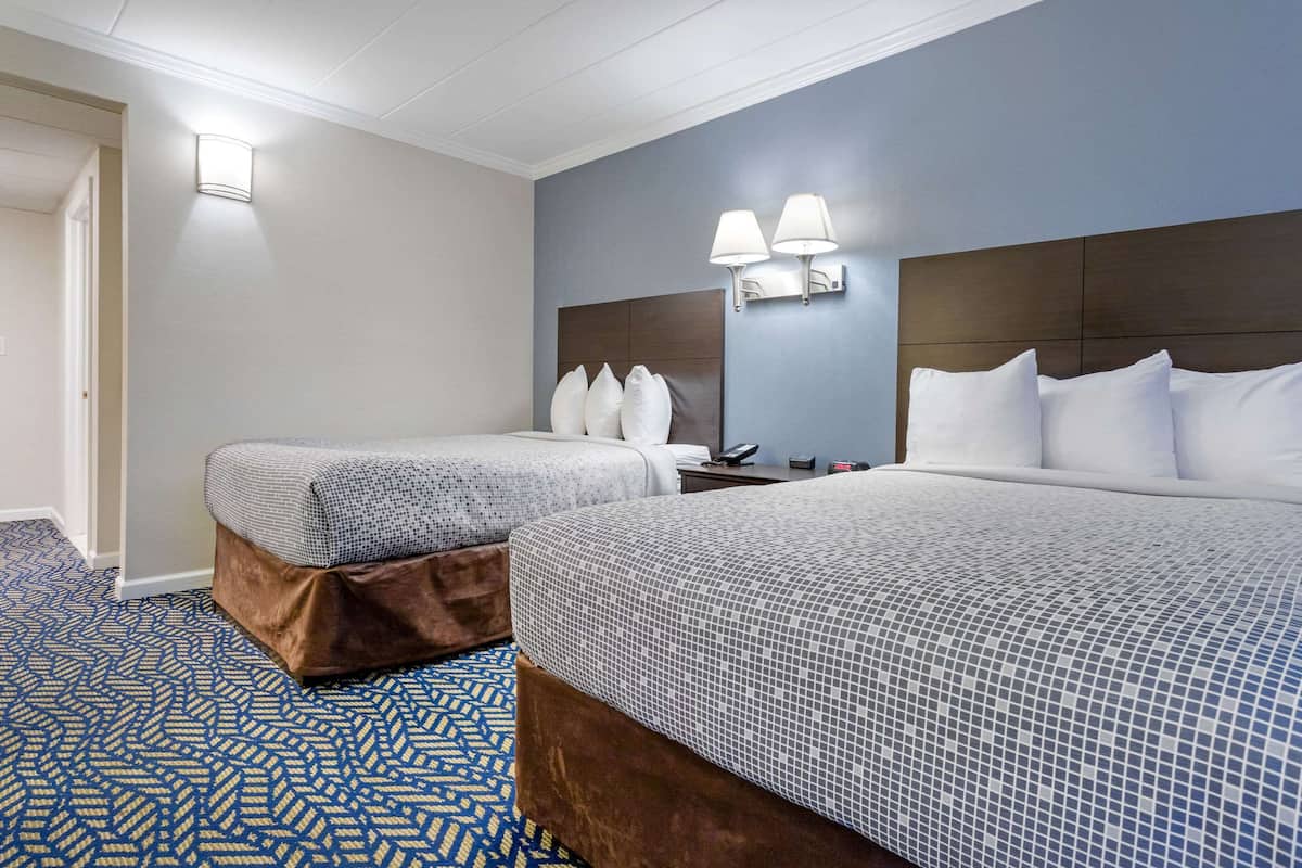 A hotel room with two beds, a patterned carpet, and a wall-mounted lamp.