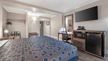 Habitación de hotel con cama, escritorio, silla, televisor de pantalla plana, microondas, refrigerador y baño con toallero y retrete.