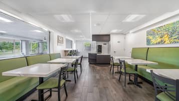 L’intérieur d’un restaurant, avec des banquettes et des tables, un espace cuisine et une vue par les fenêtres.