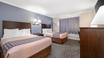 Quarto de hotel com duas camas, mesa de cabeceira, luminária, aparelho de ar condicionado e janela com cortinas.