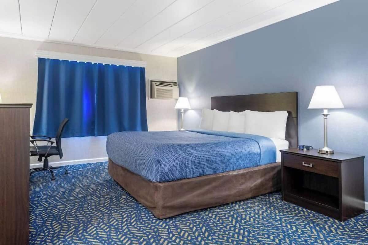 A hotel room with a bed, two bedside lamps, a desk, and a chair.
