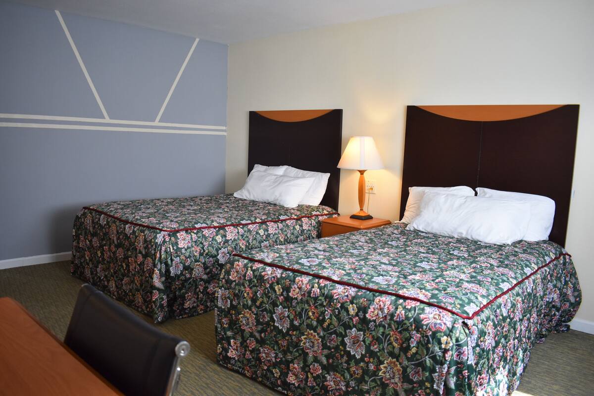 A hotel room with two single beds, a wooden desk, and a chair.