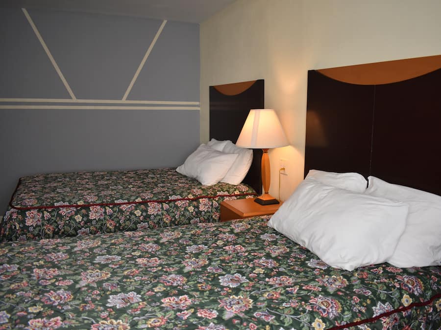 Une chambre d’hôtel avec deux lits, chacun agrémenté d’une literie à motifs floraux, une table de chevet avec une lampe et une tête de lit au design incurvé.