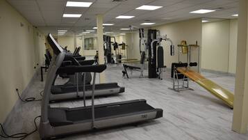 Une salle de sport équipée de tapis de course, d’appareils de musculation et d’un banc.