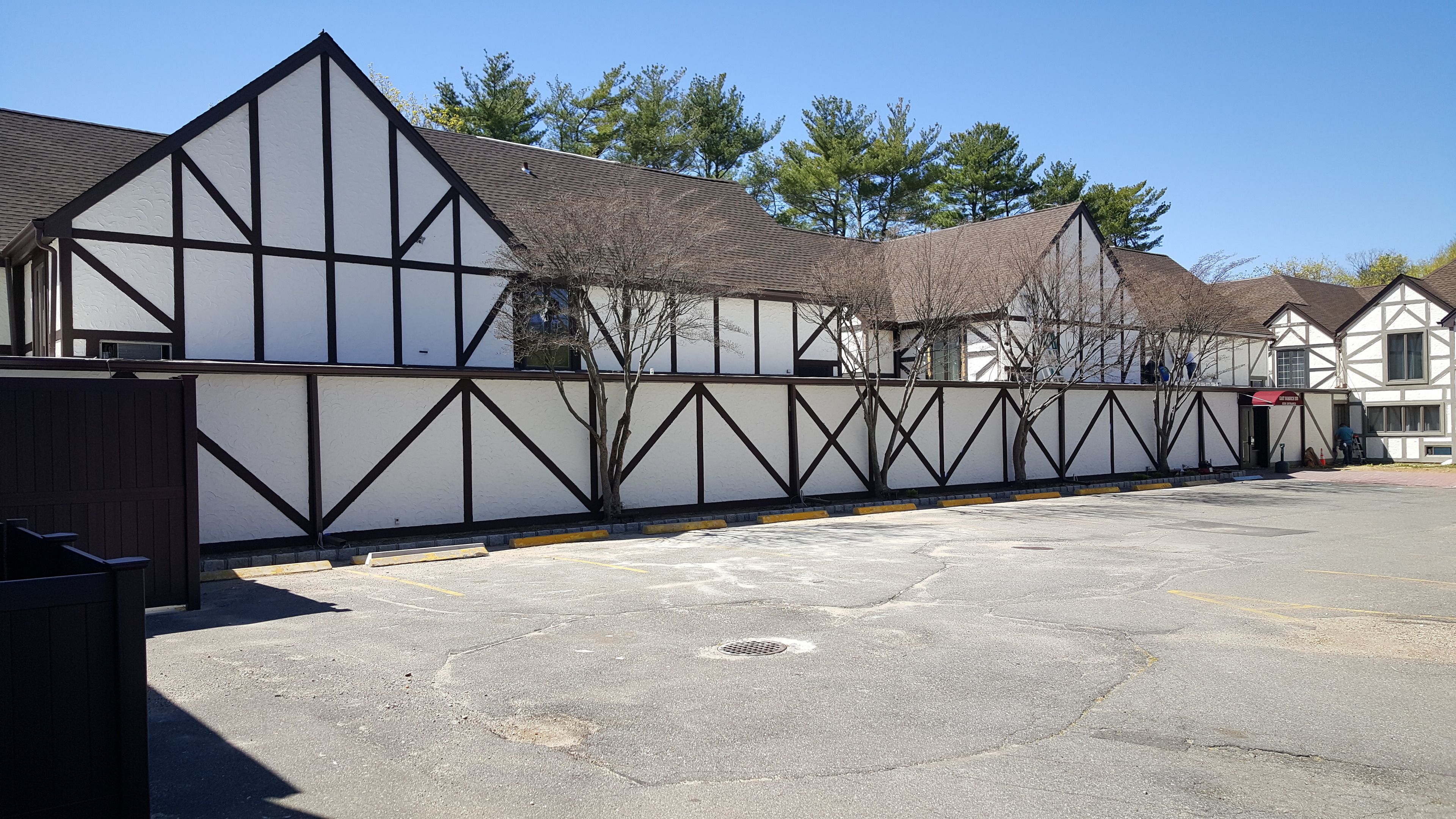 A row of traditional half-timbered buildings with a gated entrance and a paved parking area.