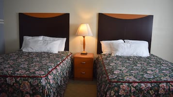 Habitación de hotel con dos camas individuales, cada una con cubrecama floral y almohadas blancas. Hay una mesita de noche de madera con una lámpara entre las camas.