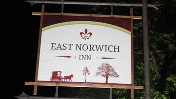 Letrero del East Norwich Inn con un carruaje tirado por caballos y árboles.