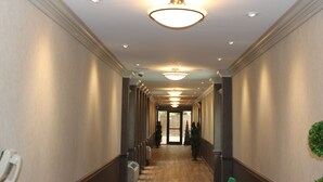 A long, narrow hallway with a series of recessed lights on the ceiling, a central door at the end, and a radiator on the left wall. - East Norwich Inn (East Norwich)