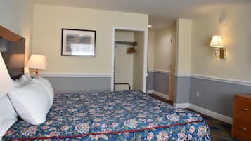 Quarto de hotel com uma cama, uma mesinha de cabeceira, uma luminária, um quadro na parede e uma porta que dá para o banheiro.