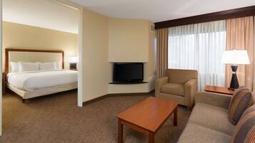 A hotel room with a bed, a television, a sofa, a coffee table, and a chair.