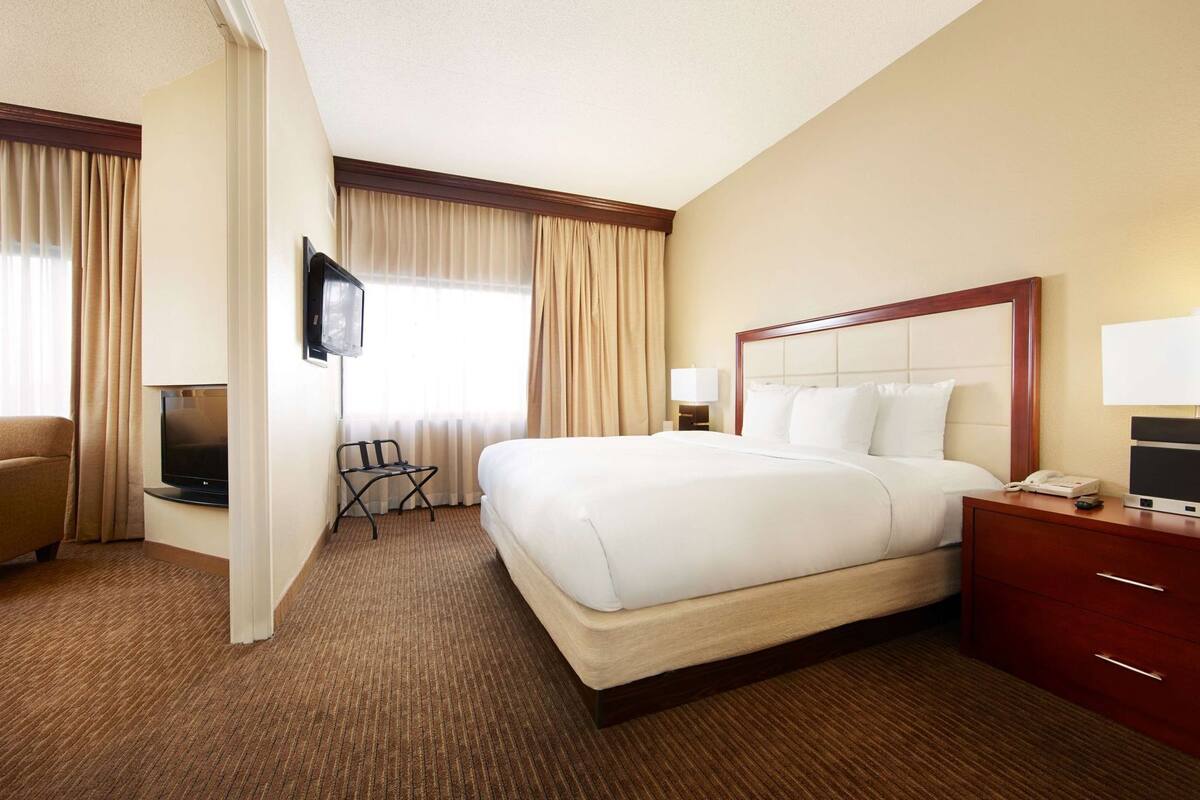 A hotel room with a bed, a TV, a desk, a chair, and a window with curtains.