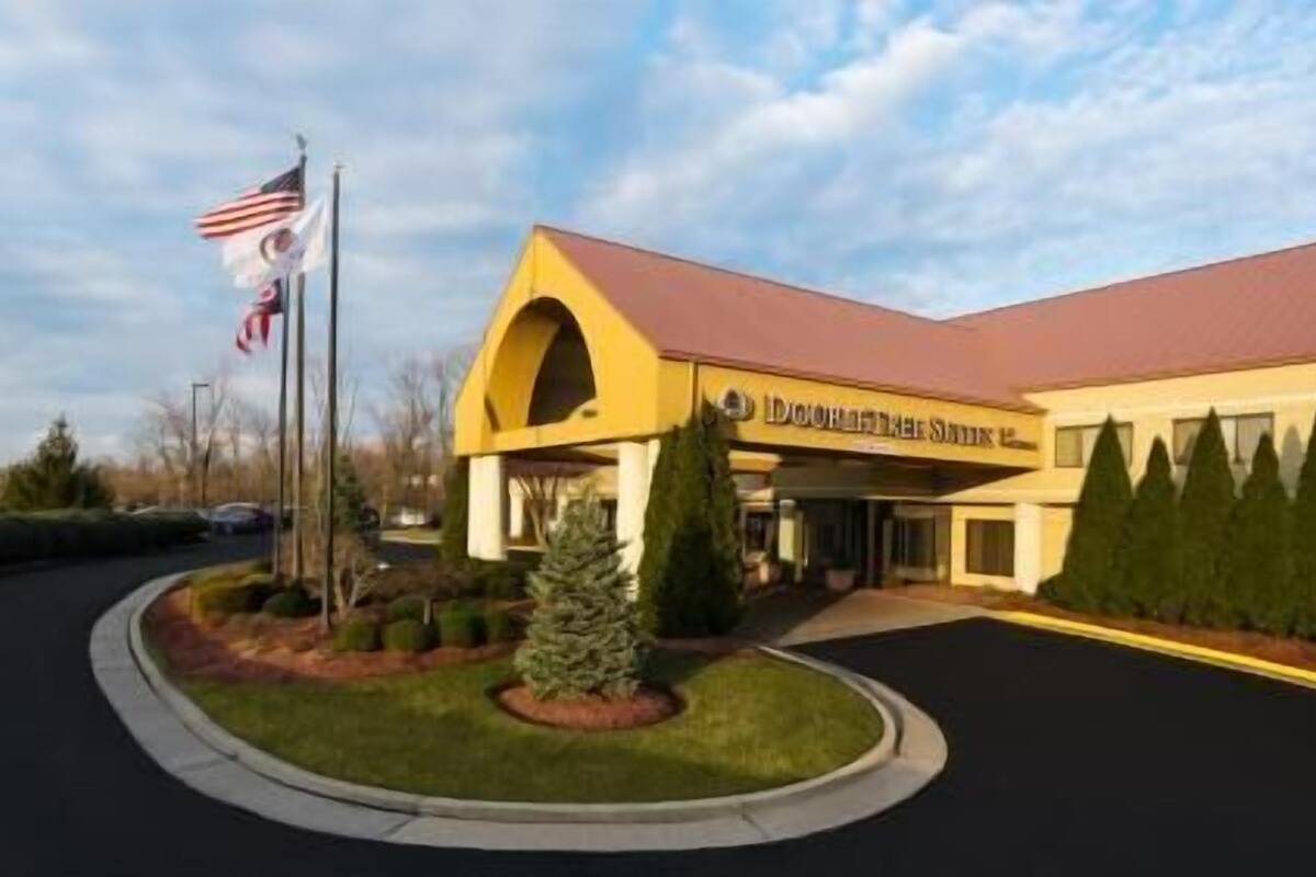 A hotel with a yellow facade, an American flag, and a well-maintained lawn.