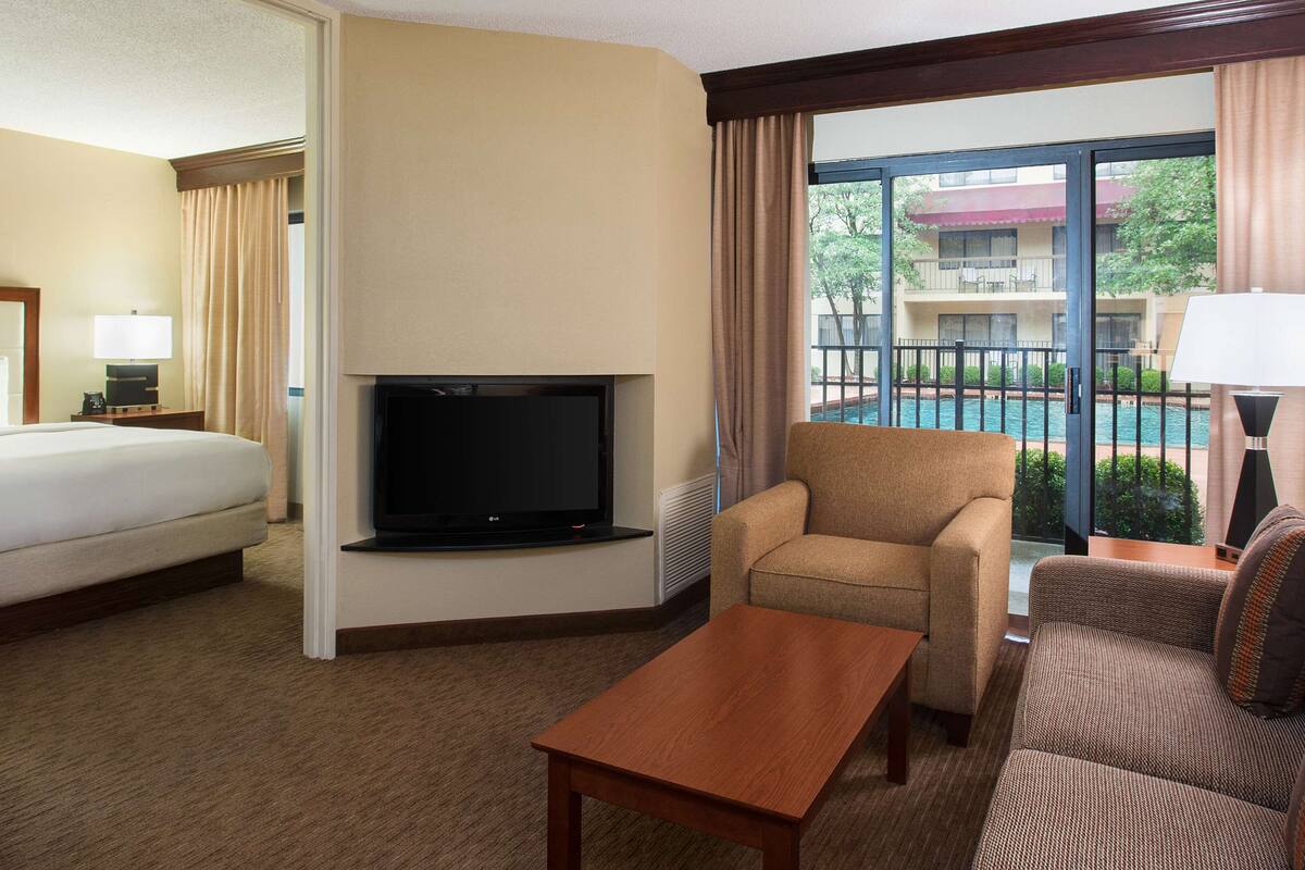 A hotel room with a bed, a TV, a sofa, a chair, and a view of a pool.