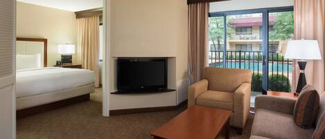 Ein Hotelzimmer mit Bett, Fernseher, Sofa, Sessel und Blick auf einen Pool.