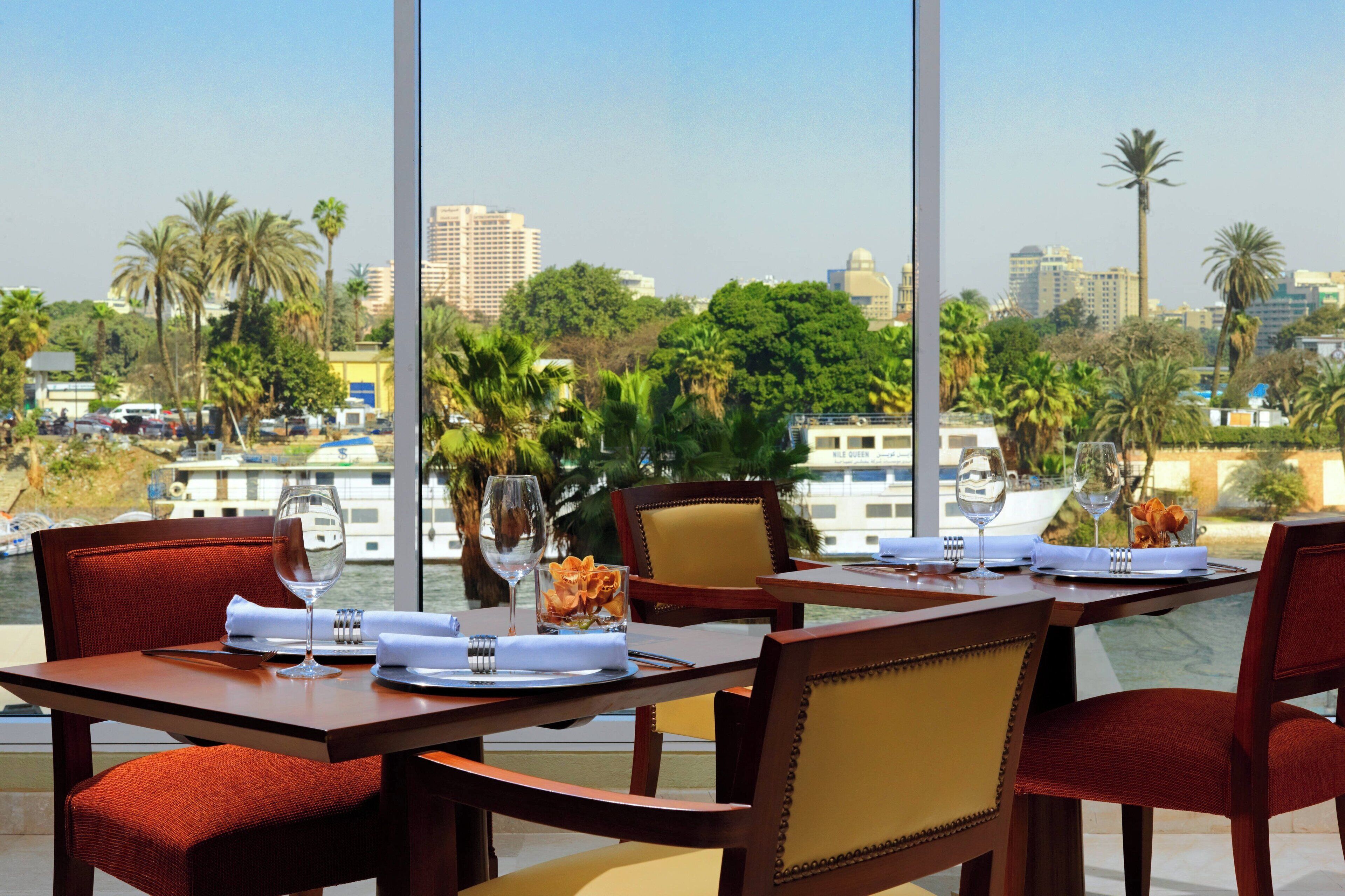 A dining table set with chairs, a view of a cityscape, and palm trees.