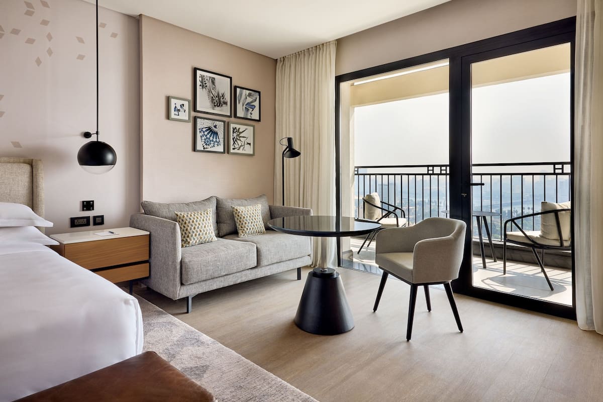 Habitación de hotel moderna con cama, sofá, una mesa redonda y un balcón con vistas.