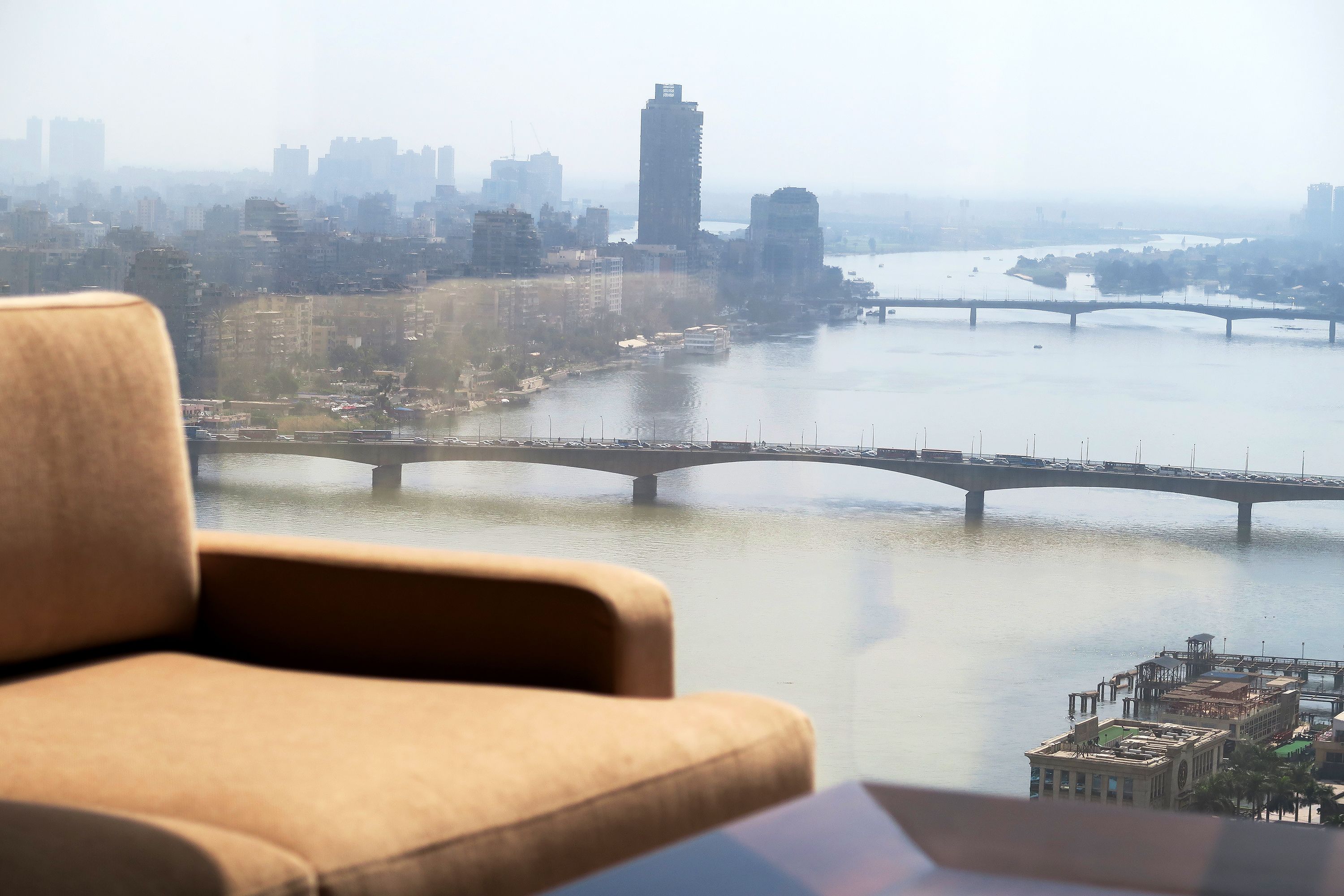A view from a high vantage point overlooking a river with bridges, a cityscape in the background, and a sofa in the foreground.