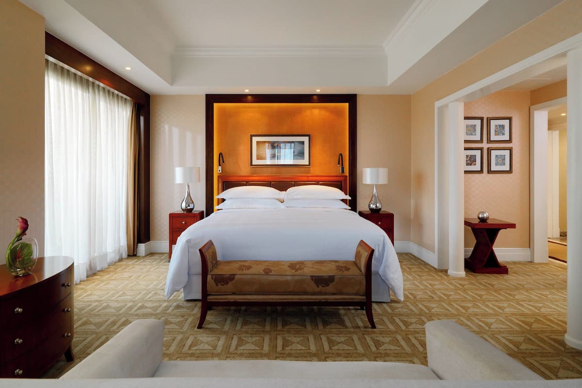 Una habitación de hotel con una cama grande, un banco, un aparador y una mesita de noche con lámparas.